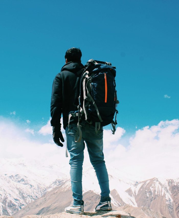 A lone hiker with a backpack surveys snow-capped mountains under a clear blue sky.
